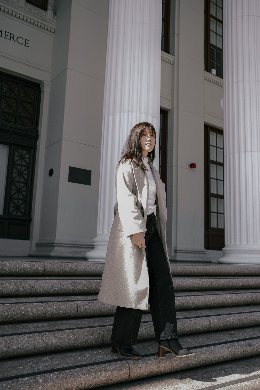 Black denim pants with a beige oversized wool coat